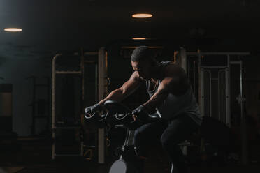 Serious black man on exercise bike in gym - ADSF00650