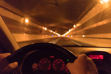 Die Hände eines Menschen am Lenkrad eines Autos in einem Tunnel mit beleuchteten Lampen in den Pyrenäen - ADSF00658
