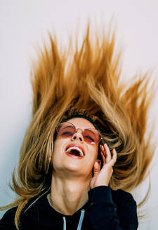 Junge blonde Frau in schwarzem Pullover und Sonnenbrille mit langen Haaren tanzt im Studio und lächelt auf weißem Hintergrund - ADSF00727