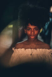 Ernste, schöne afroamerikanische Frau mit Piercing und Afrofrisur, die im Dunkeln steht und in die Kamera blickt - ADSF00810