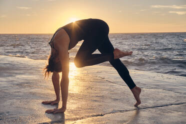 Junge Frau in Downward Facing Dog Pose am Meer - ADSF00895