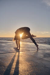 Junge Frau in Downward Facing Dog Pose am Meer - ADSF00896