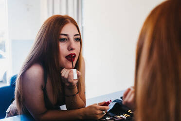 Reflection of young charming woman holding red lipstick and doing makeup - ADSF00902