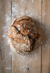 Ein kreisförmiger Laib Roggenbrot liegt auf einem Holztisch mit Mehl - ADSF00908