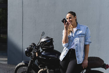 Smiling woman sitting on motorbike and using smartphone - FMOF01025