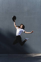 Woman with motorcycle helmet jumping in front of grey wall - FMOF01034