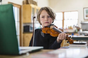 Six year old boy playing violin, having a remote video lesson in lockdown at home. - MINF14613
