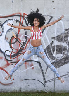 Young woman jumping in front of wall with graffiti - PGCF00078