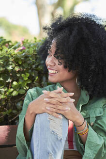 Smiling woman sitting on bench and looking sideways - PGCF00083