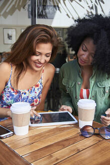 Freundinnen mit Kaffee zum Mitnehmen und Tablet im Cafe - PGCF00090