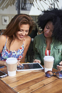 Girlfriends with coffee to go using tablet in cafe - PGCF00090