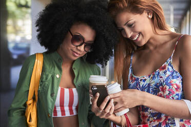 Freundinnen mit Kaffee zum Mitnehmen per Smartphone - PGCF00093