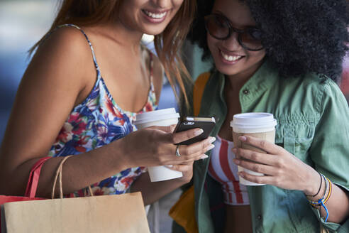 Freundinnen mit Kaffee zum Mitnehmen per Smartphone - PGCF00094