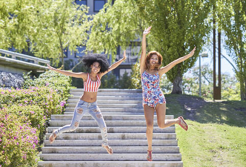 Girlfriends jumping from stairs in park - PGCF00100