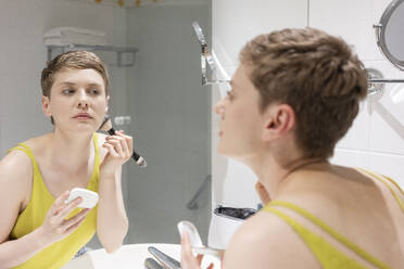 Schöne Frau mit kurzen Haaren trägt Make-up auf, während sie ihr Spiegelbild im Badezimmer betrachtet - TAMF02487