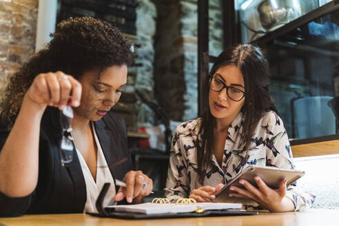 Businesswomen discussing over diary while planning at cafe - MTBF00527