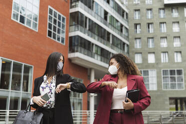 Young multi-ethnic female colleagues giving elbow bump against building in city - MTBF00539