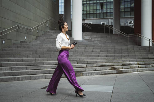 Modische junge Geschäftsfrau beim Spazierengehen mit Tagebuch in der Stadt - MTBF00545