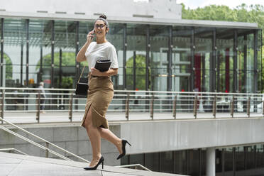 Female professional talking through mobile phone on steps in city - MTBF00549