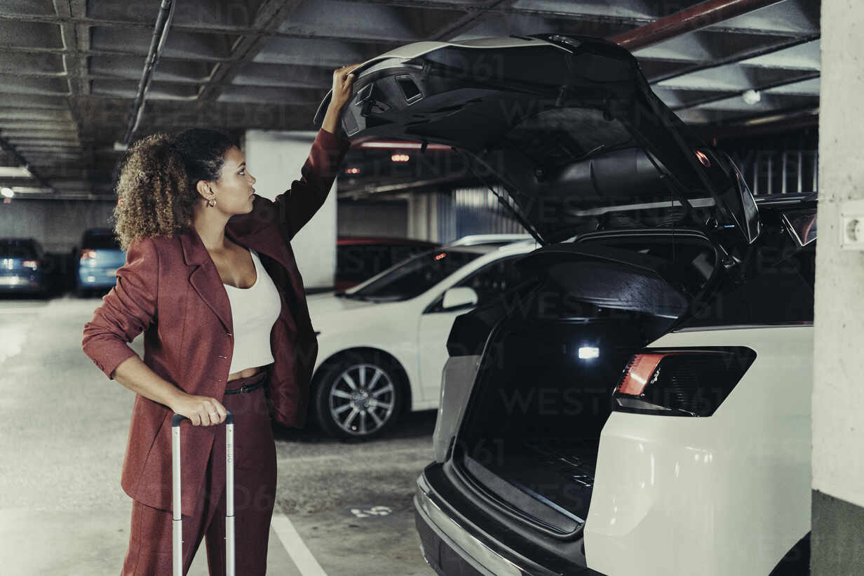 Junge berufstätige Frau auf Geschäftsreise schließt Kofferraum im Parkhaus,  lizenzfreies Stockfoto
