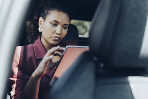 Junge Geschäftsfrau, die im Auto sitzend ein digitales Tablet benutzt - MTBF00559