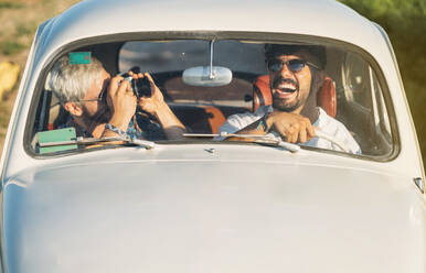 Zwei fröhliche junge Leute mit Kamera fahren Retro-Auto und machen Bilder während der Reise in der Landschaft zusammen - ADSF01027