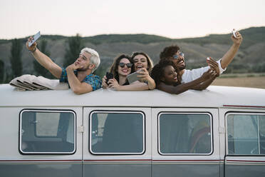 Gruppe von fröhlichen verschiedenen Menschen stehen in Oldtimer-Van mit geöffnetem Dach und posieren für Selfie während der Reise in der Landschaft zusammen - ADSF01052
