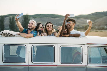 Gruppe von fröhlichen verschiedenen Menschen stehen in Oldtimer-Van mit geöffnetem Dach und posieren für Selfie während der Reise in der Landschaft zusammen - ADSF01053