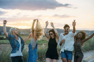 Gruppe junger Leute in legerer Kleidung, die lachen und tanzen, während sie Spaß in der schönen Landschaft haben - ADSF01057