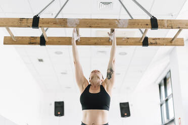 Starke Frau in Sportkleidung, die sich im Fitnessstudio an ein Holzbrett hängt und sich hochzieht - ADSF01089