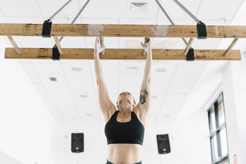 Starke Frau in Sportkleidung, die sich im Fitnessstudio an ein Holzbrett hängt und sich hochzieht - ADSF01089