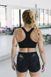 Back view of anonymous female athlete with hands covered with chalk standing in gym during training - ADSF01091