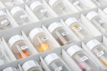 Blick von oben auf viele Plastikgefäße mit Nummern und bunten Pillen, die in einer weißen Papierschachtel liegen, im Weichzeichner - ADSF01103