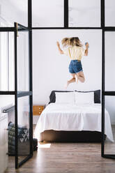 Excited woman with phone jumping on bed - ADSF01165