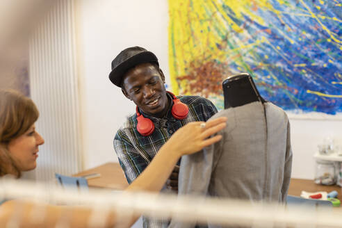 Lächelnder junger Mann betrachtet Modedesigner, der eine Schaufensterpuppe im Designstudio hält - EIF00067