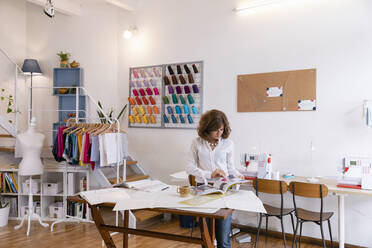 Weibliche Modeunternehmerin sieht sich eine Zeitschrift an, während sie an einer Werkbank im Designstudio steht - EIF00071