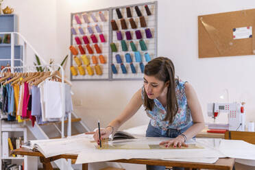 Schöne junge weibliche Designpraktikantin zeichnet auf Papier an der Werkbank im Atelier - EIF00075