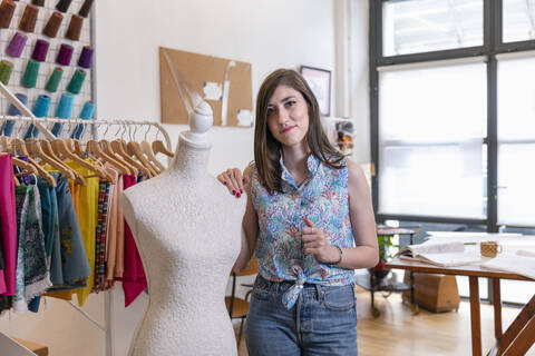 Confident young female fashion trainee standing by dressmaker's dummy at design studio stock photo