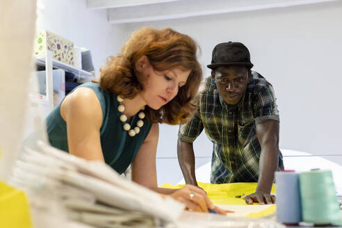 Young male trainee looking at fashion designer drawing on fabric - EIF00090