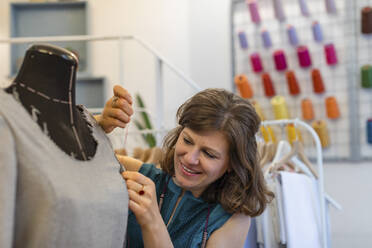 Lächelnde Modedesignerin näht ein Kleid an einer Puppe im Designstudio - EIF00095
