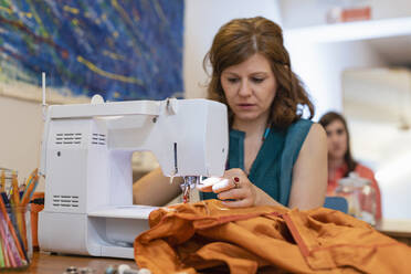 Näherin näht orangefarbenen Stoff auf einer Maschine in einem Modeatelier - EIF00101