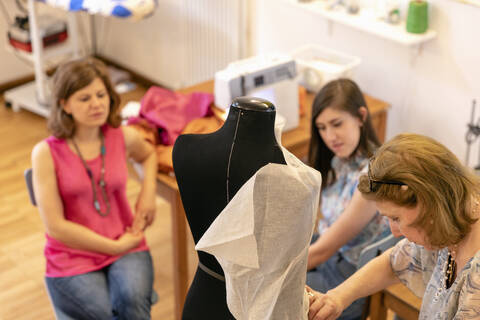 Female professionals looking at senior designer working on mannequin in studio stock photo