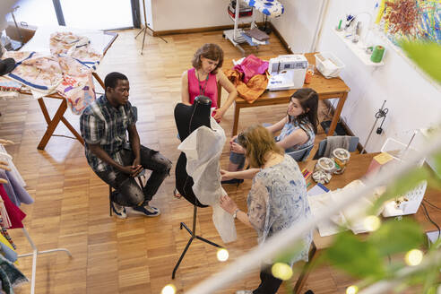 Coworkers looking at senior designer working on mannequin in atelier - EIF00108