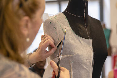 Close-up of senior designer cutting fabric on mannequin with scissors in atelier - EIF00110