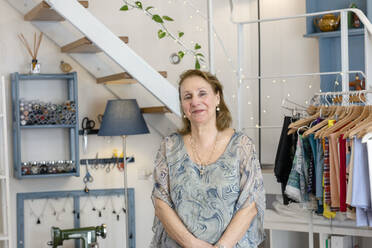 Smiling senior female design professional standing at illuminated fashion studio - EIF00111