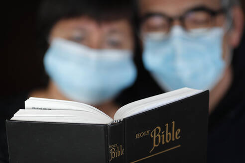Man and woman reading the bible with a disposable mask to avoid contagious coronavirus (COVID-19), France, Europe - RHPLF15392