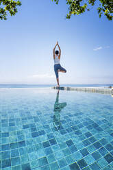 Eine junge Frau übt Yoga neben einem Infinity-Pool, Candidasa, Bali, Indonesien, Südostasien, Asien - RHPLF15426