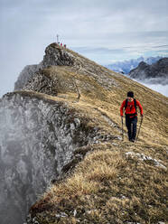 Mann beim Wandern mit Stöcken auf einem Berggipfel bei nebligem Wetter - MALF00016