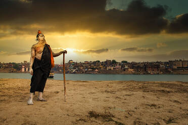 Ein indischer Hindu-Sadhu (Heiliger) am Ufer des heiligen Flusses Ganges und die Stadt Varanasi im Hintergrund, Varanasi, Uttar Pradesh, Indien, Asien - RHPLF15811