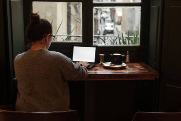 Ein junger Student arbeitet an einem Tisch in der Nähe eines Kneipenfensters - CAVF86870